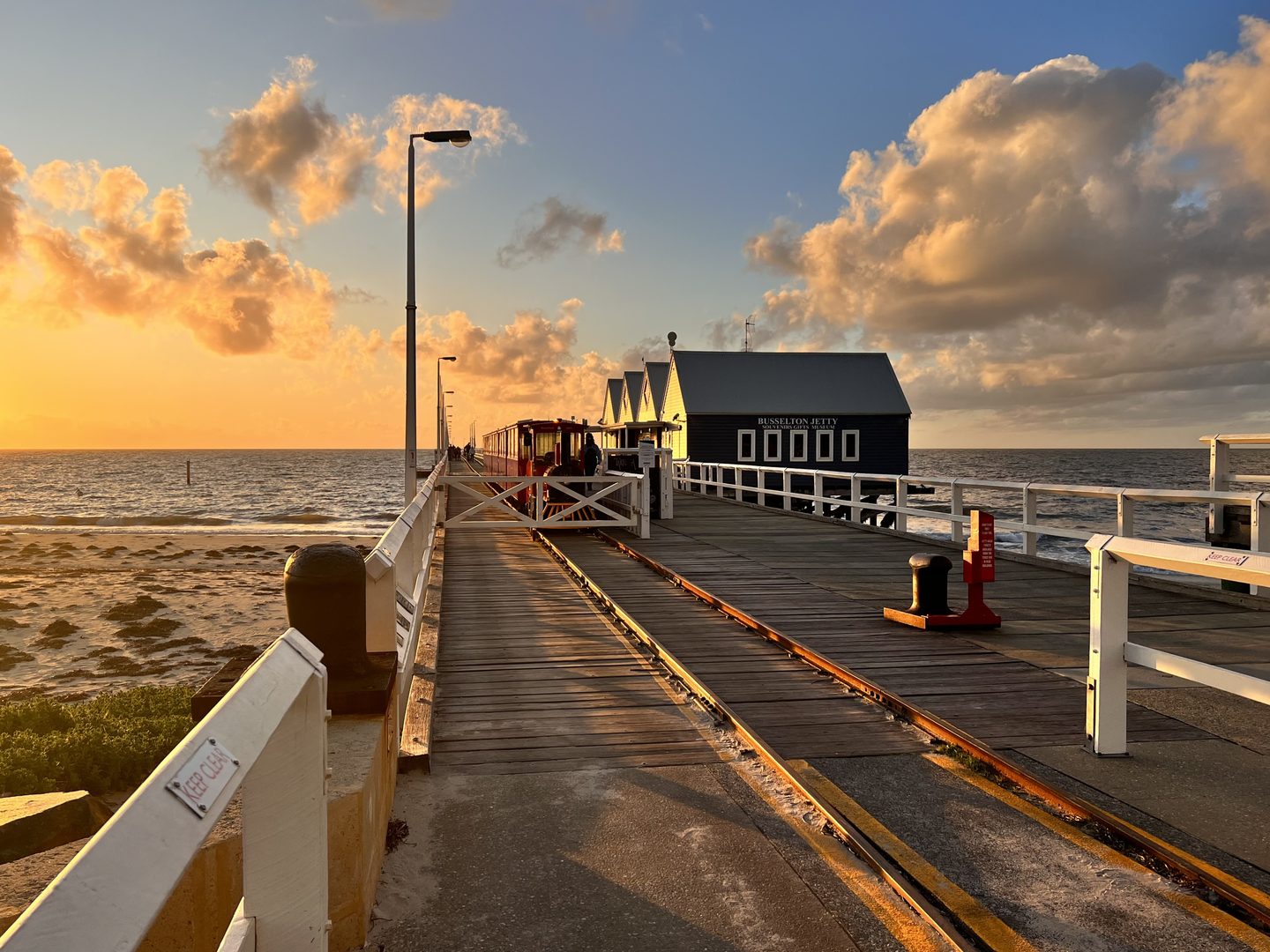 Tief stehende Sonne beleuchtet die Gleise und blauen Gebäude am Busselton Jetty.