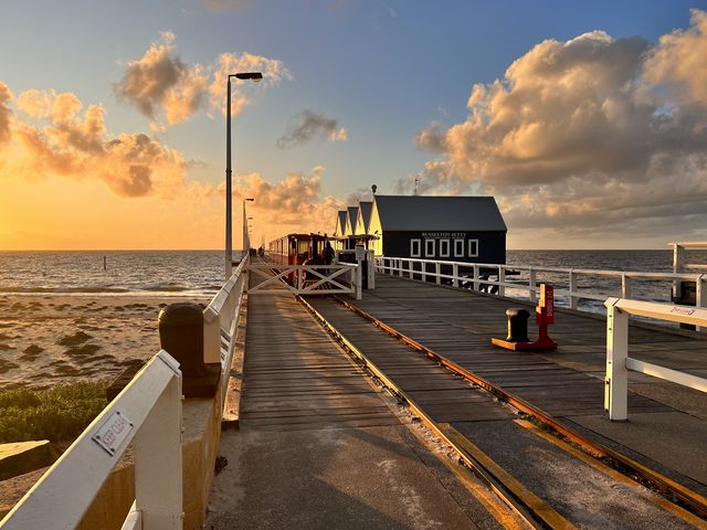 Low sunlight on the train rails and blue buildings at Busselton Jetty.