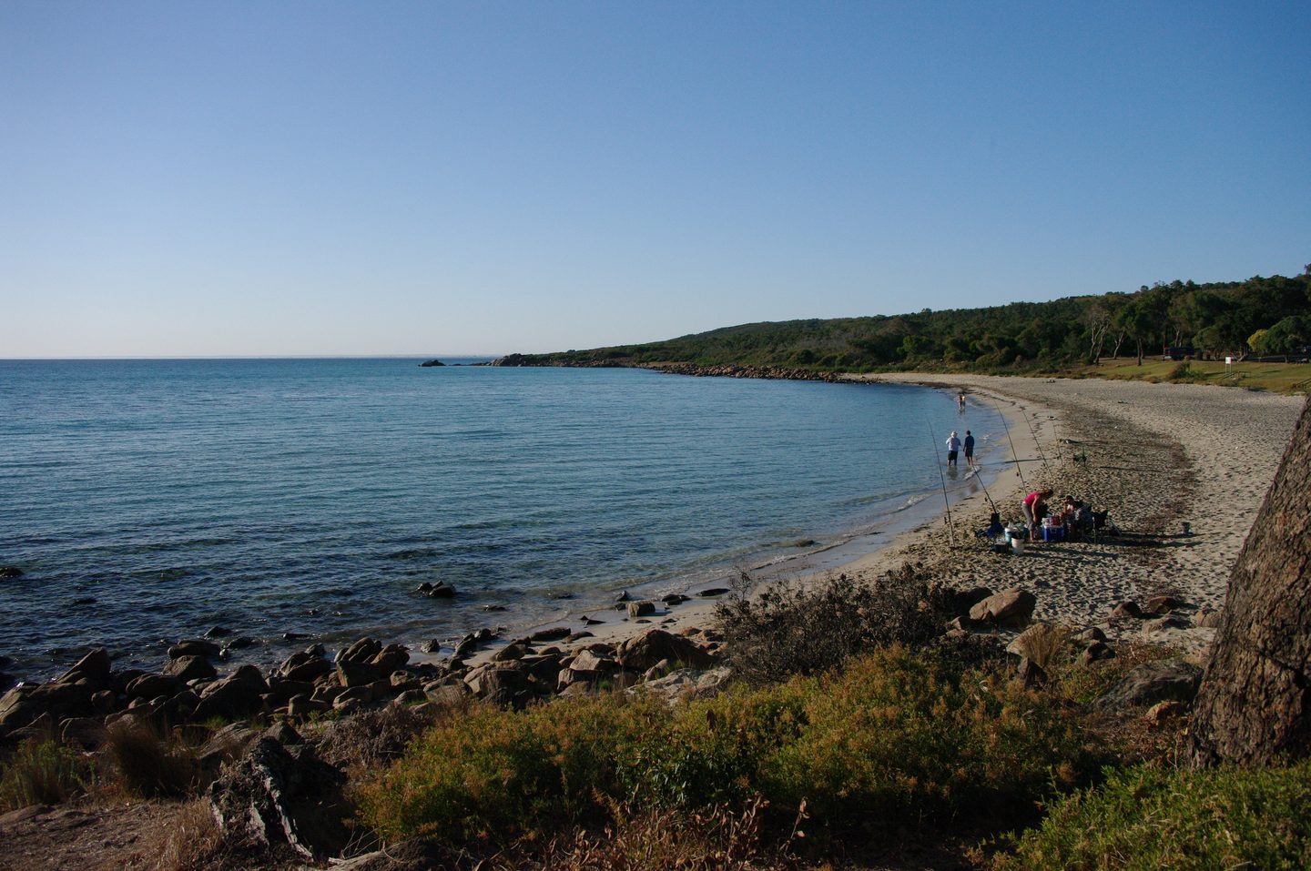 Meelup Beach an blauem Wasser, mit Felsen und Bäumen im Vordergrund.