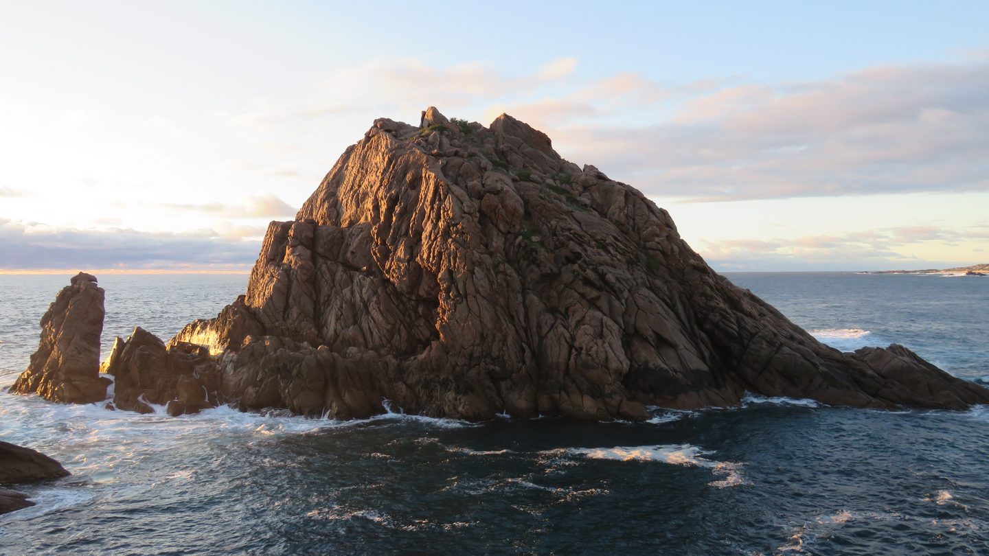 Abendlicht auf der steilen Felswand von Sugarloaf Rock, umgeben vom Meer.