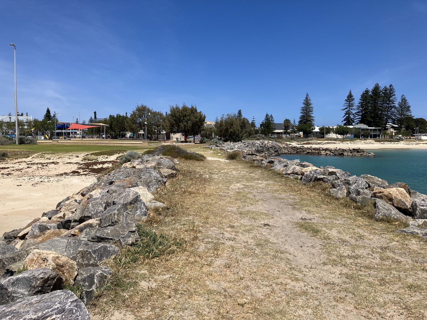 A low rock-lined path beside the water on Geraldton’s foreshore, with buildings and trees behind.