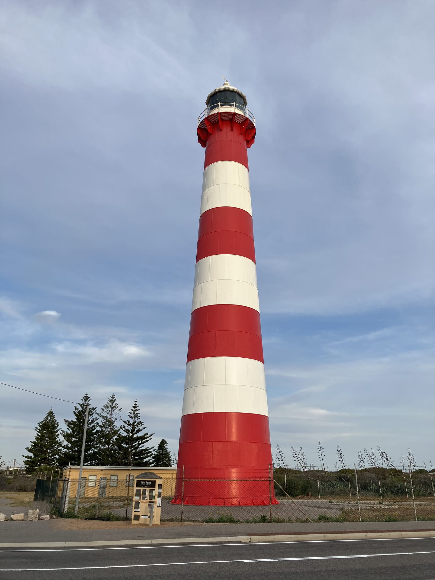 The tall Point Moore Lighthouse with red-and-white bands beside a road in Geraldton.
