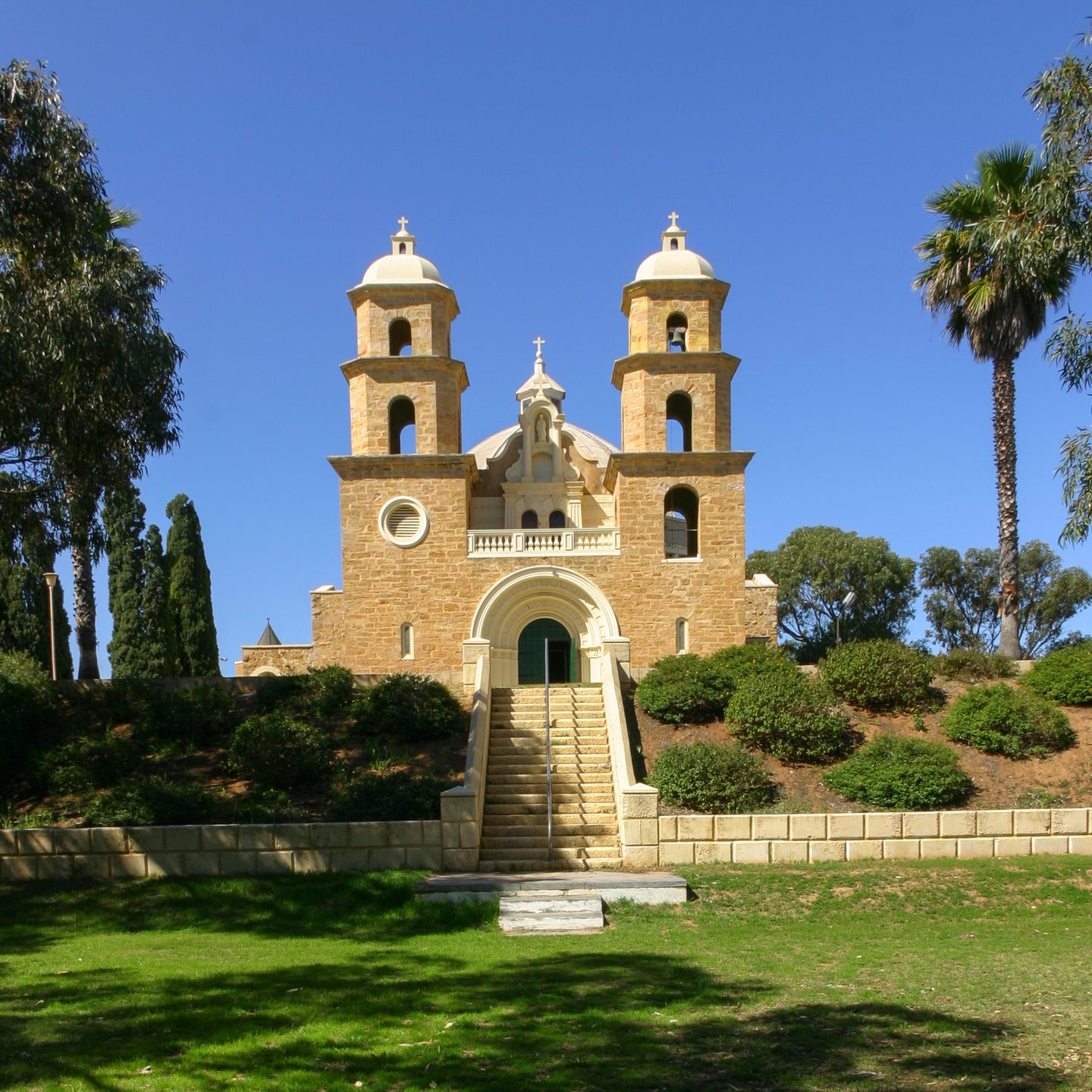 The twin towers of St Francis Xavier Cathedral above a front staircase, lawn and gardens.